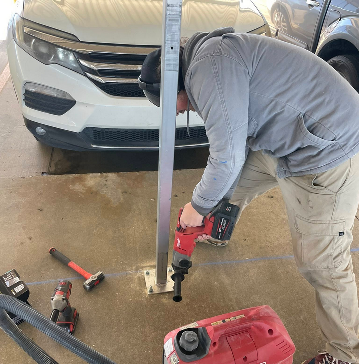 Bollard installation service - technician drilling bollard into concrete parking lot